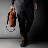 Brown leather briefcase being carried by a man wearing grey on a grey background.