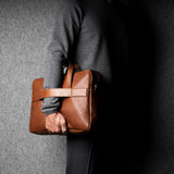 Person holding a brown leather briefcase against a gray background