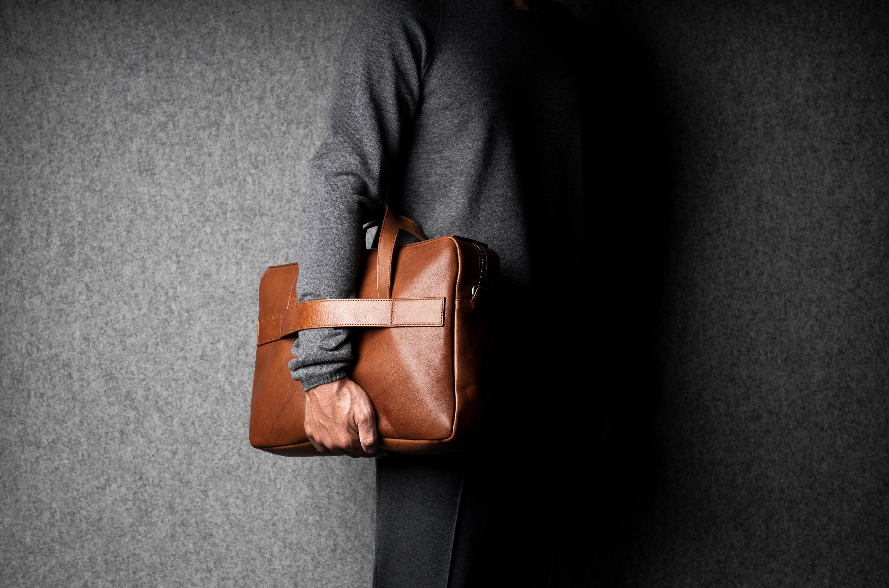 Person holding a brown leather briefcase against a gray background