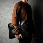 Person holding a black leather briefcase against a dark background