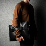 Person holding a black leather briefcase against a dark background