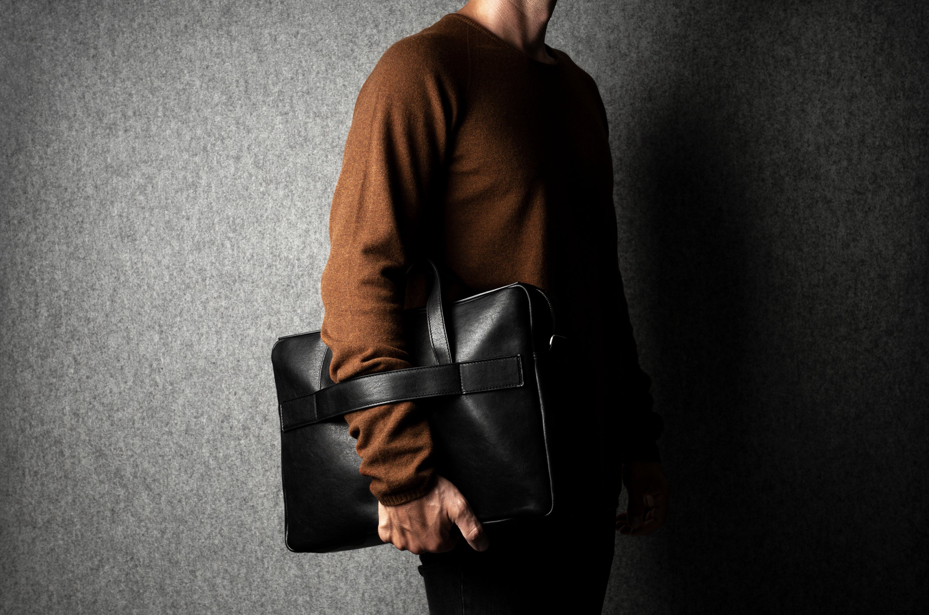 Person holding a black leather briefcase against a dark background