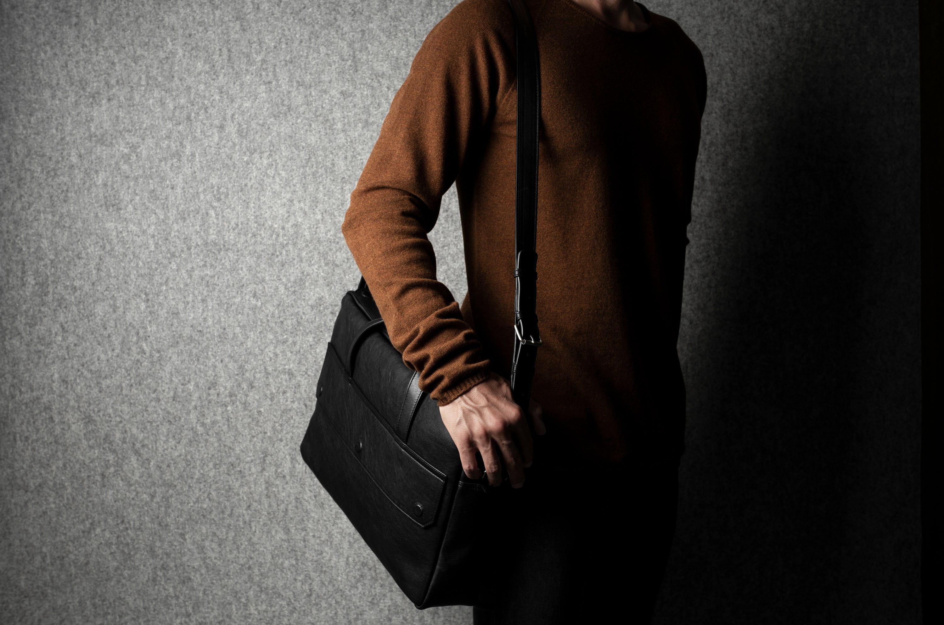 Person holding a black briefcase against a gray background