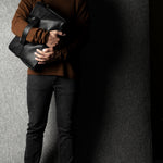 Person holding a black leather briefcase against a gray background