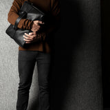 Person holding a black leather briefcase against a gray background