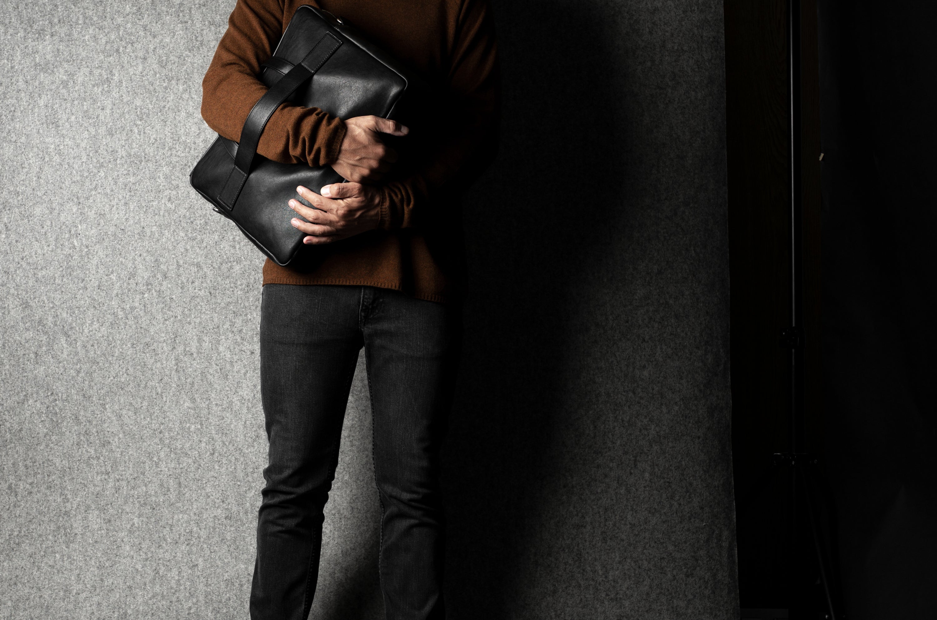 Person holding a black leather briefcase against a gray background
