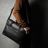 Person holding a black leather briefcase against a dark background