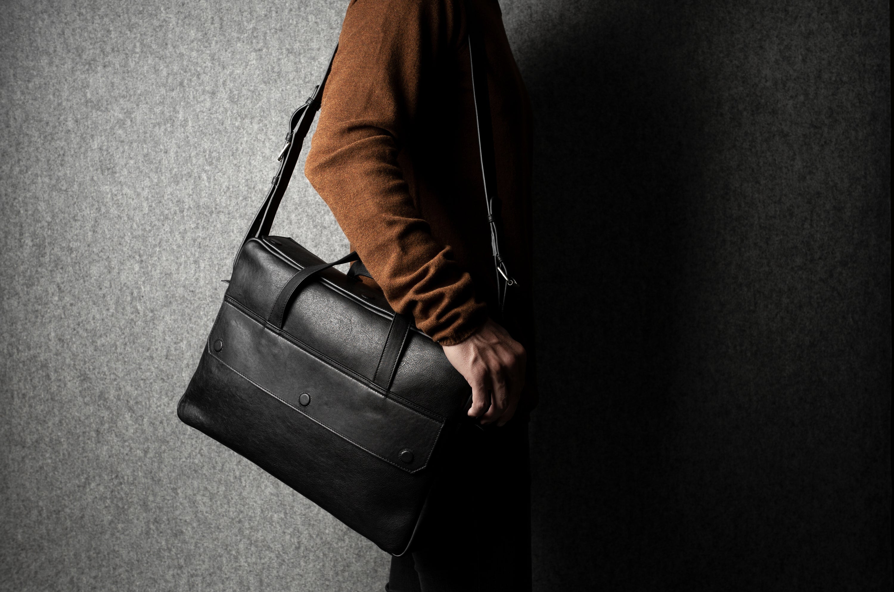 Person holding a black leather briefcase against a dark background