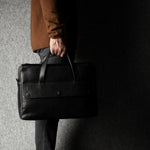 Person holding a black leather briefcase against a dark background