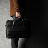 Person holding a black leather briefcase against a dark background