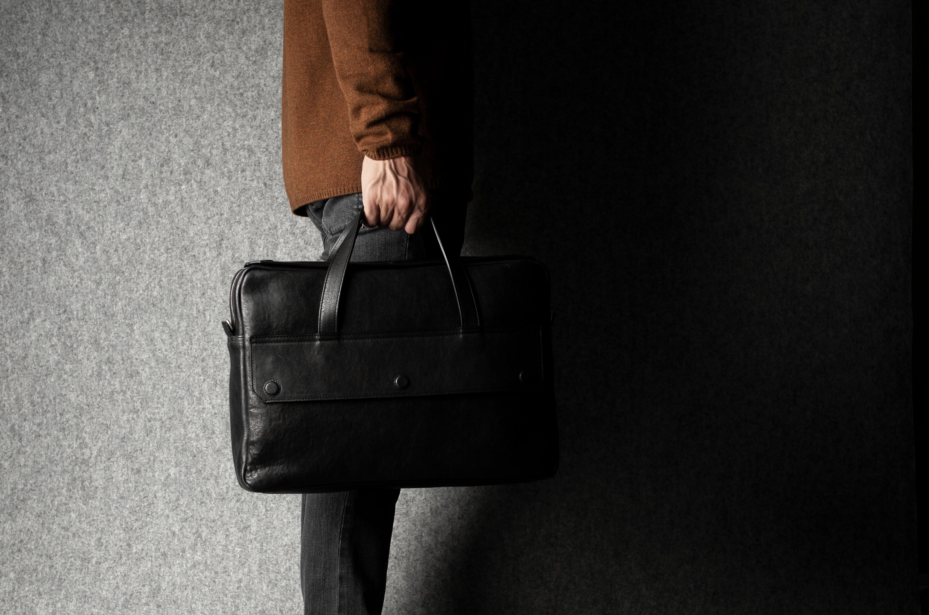 Person holding a black leather briefcase against a dark background