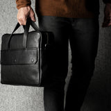 Person holding a black leather briefcase against a gray background