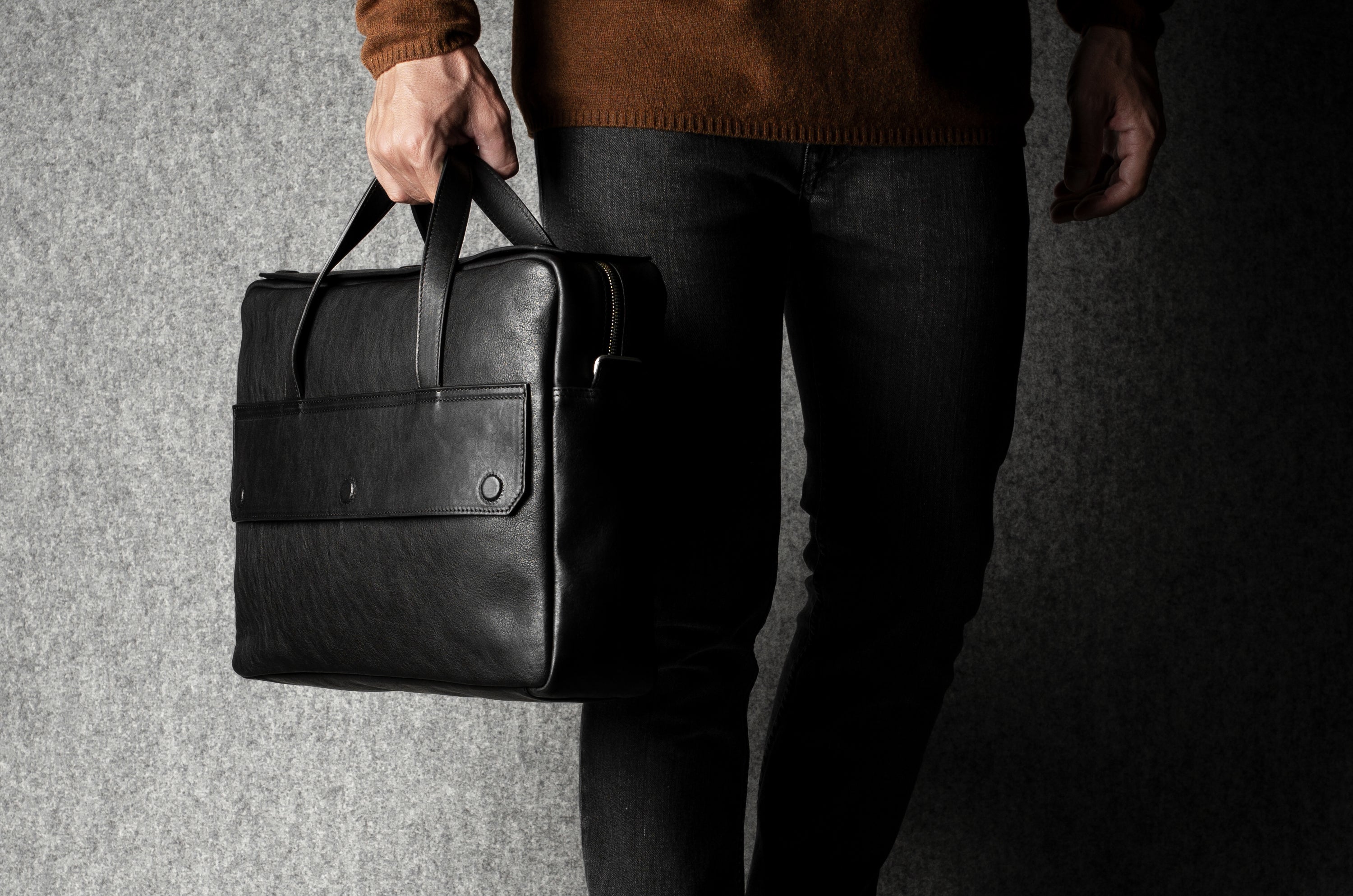 Person holding a black leather briefcase against a gray background