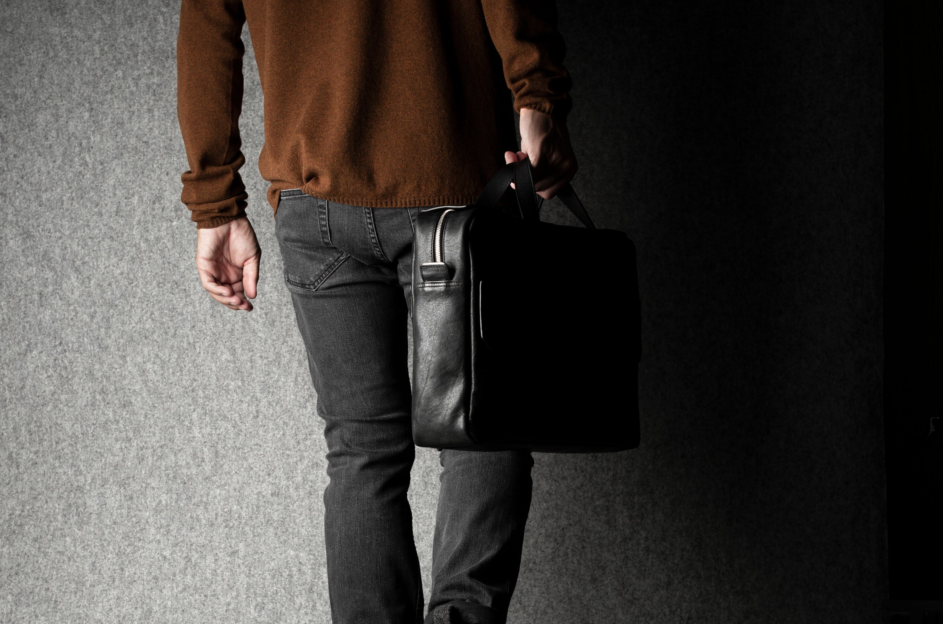 Person holding a black briefcase against a dark background