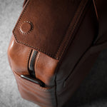 Close-up of a brown leather bag with a zipper on a gray background