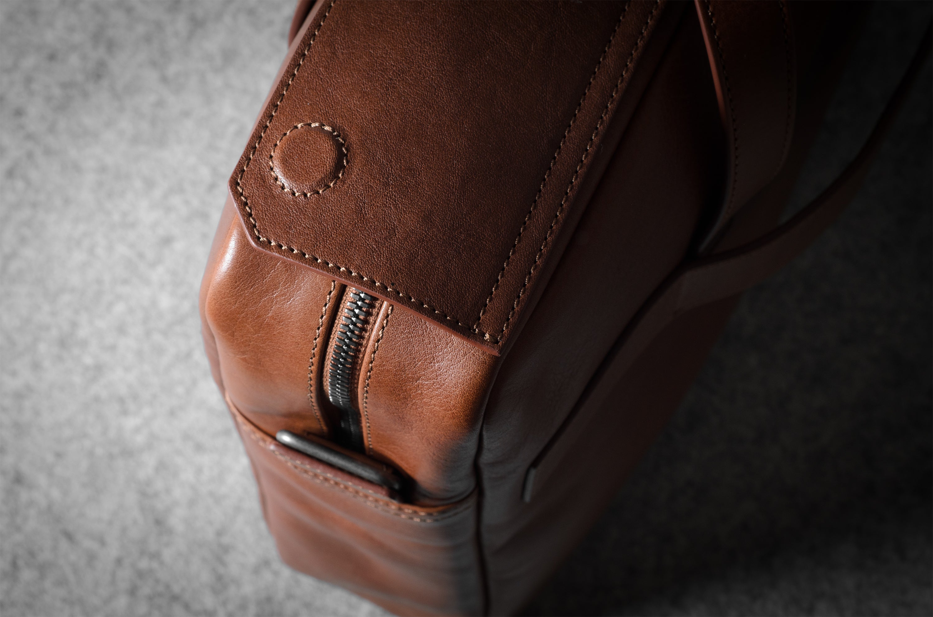 Close-up of a brown leather bag with a zipper on a gray background