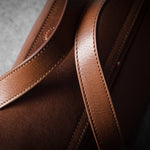 Close-up of a brown leather bag with visible stitching on a dark background