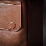 Close-up of a brown leather bag with stitching detail on a dark background
