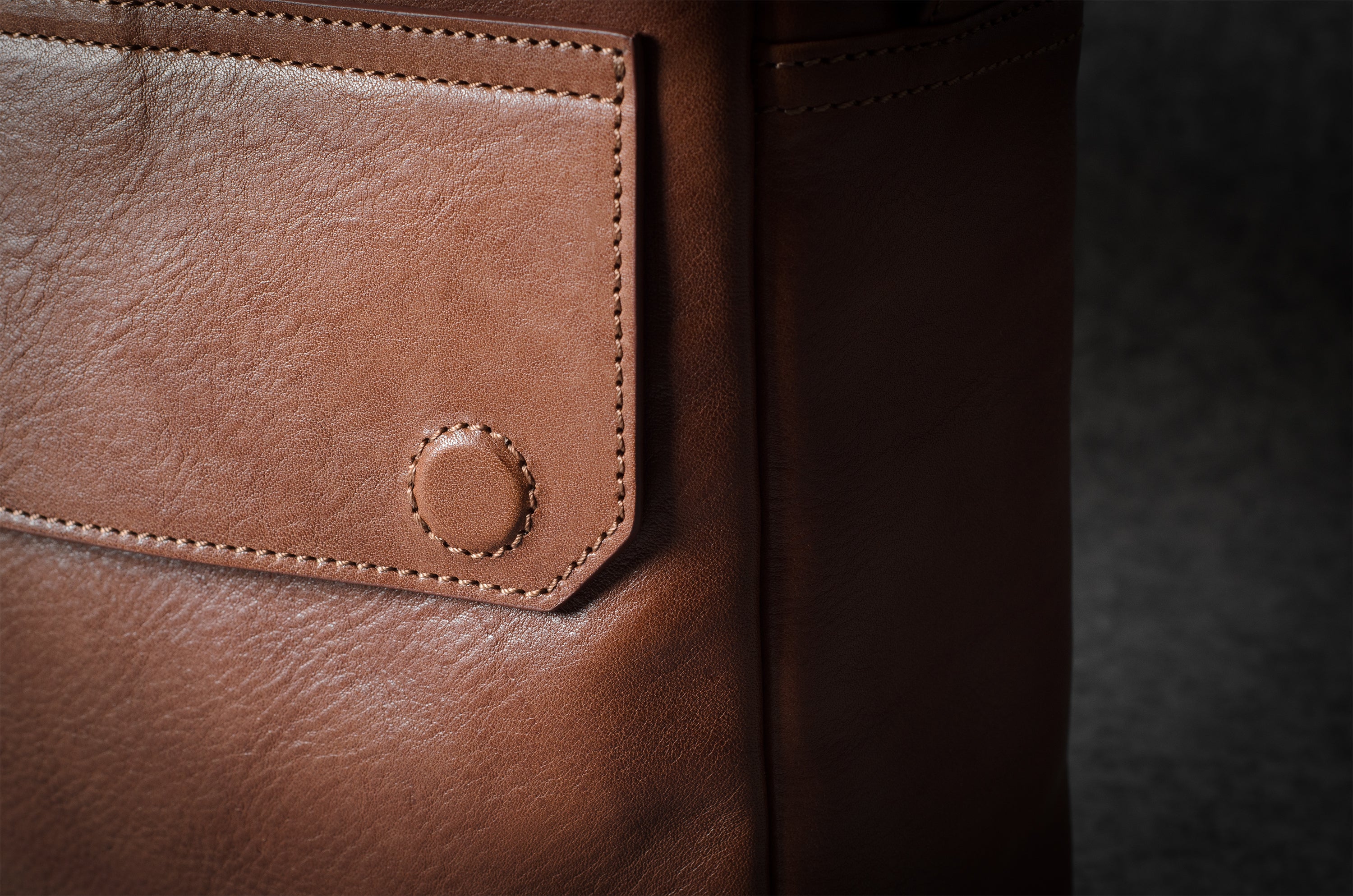 Close-up of a brown leather bag with stitching detail on a dark background