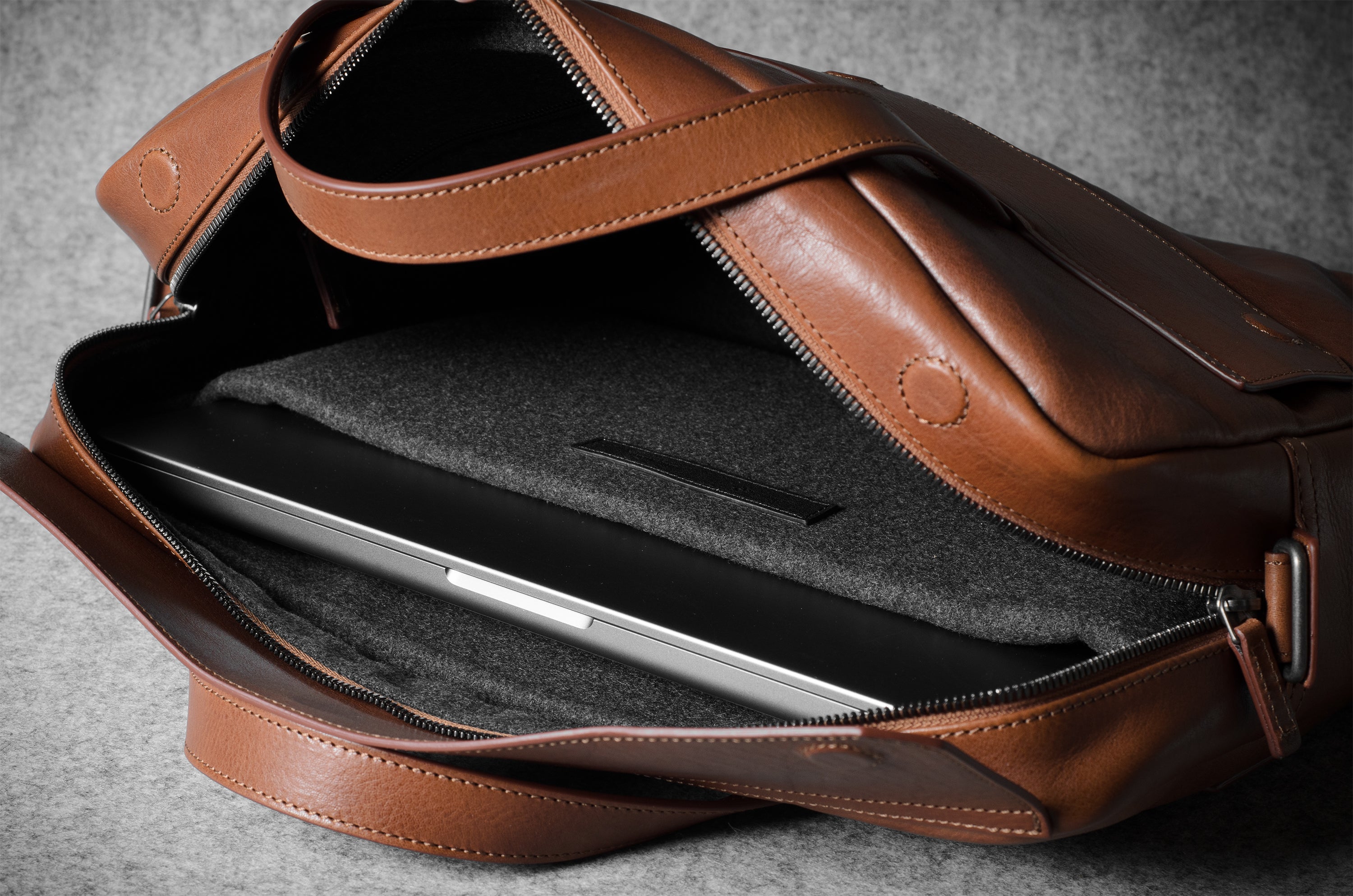 Brown leather bag with a compartment for a laptop on a gray background