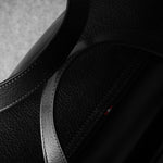 Close-up of a black leather bag with a brand logo on a gray background