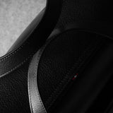 Close-up of a black leather bag with a brand logo on a gray background