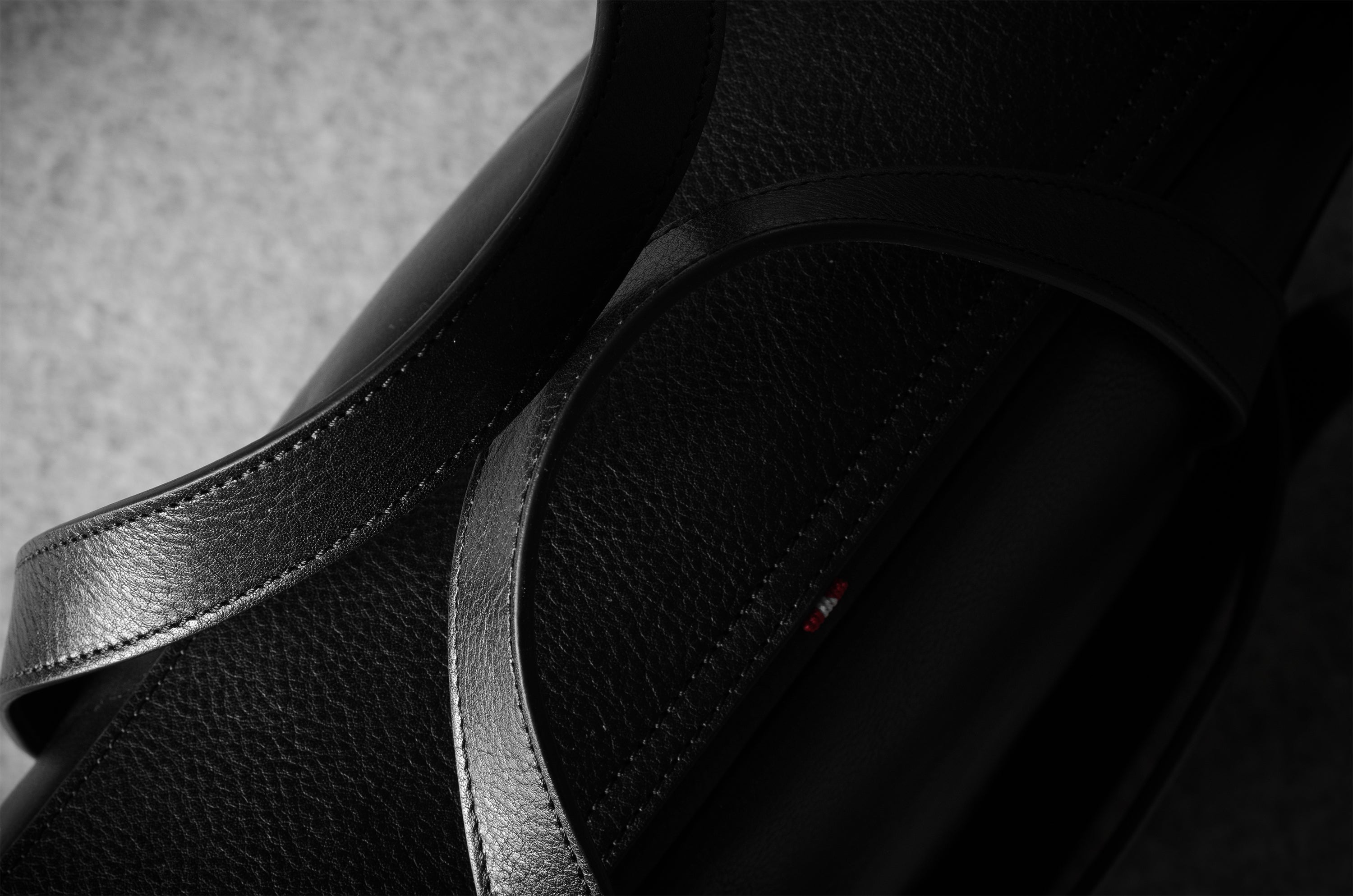 Close-up of a black leather bag with a brand logo on a gray background