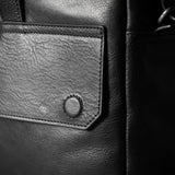 Close-up of a black leather bag with a visible brand patch.