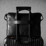 Black leather briefcase on top of a suitcase against a gray background
