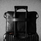 Black leather briefcase on top of a suitcase against a gray background