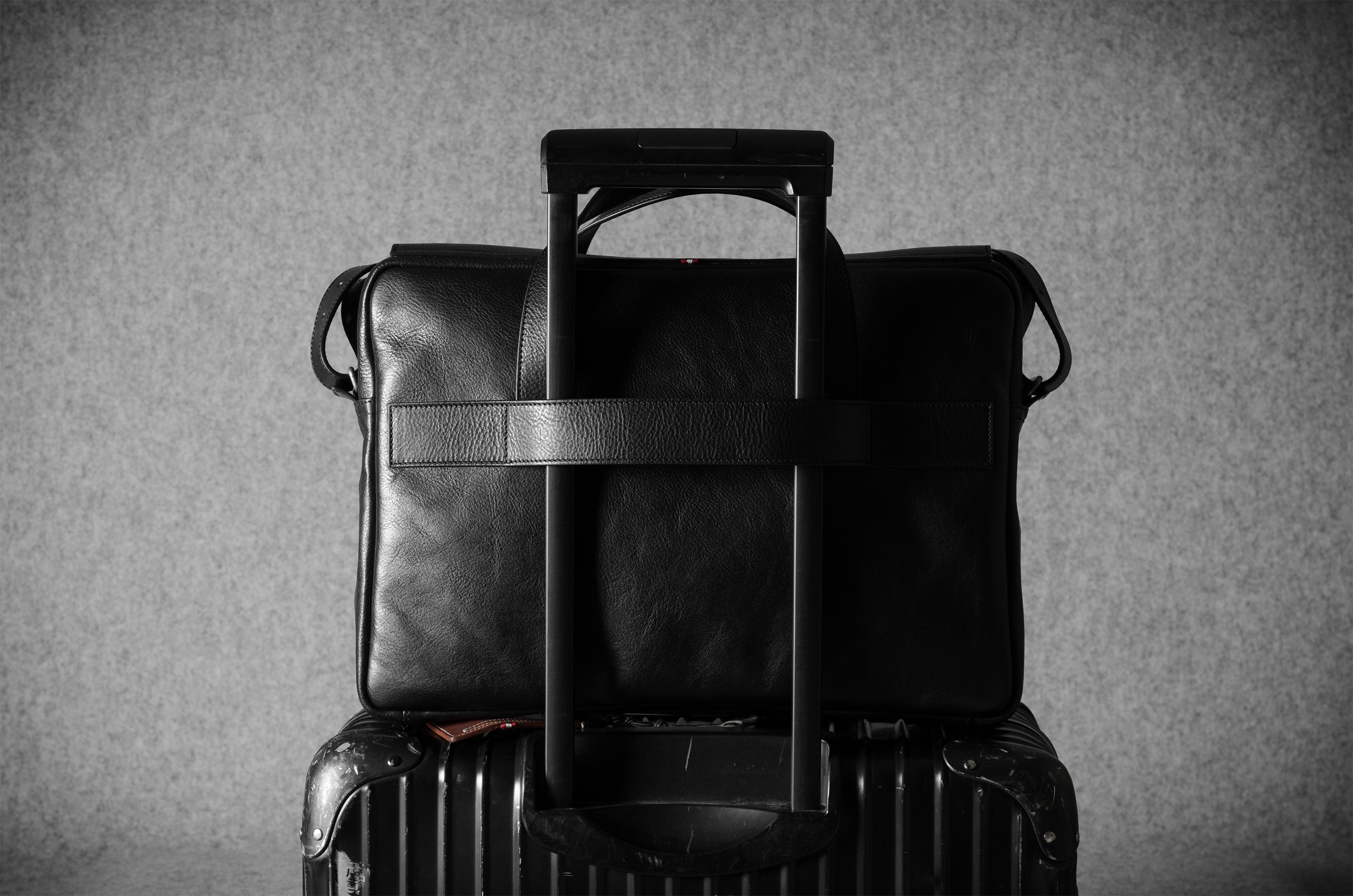 Black leather briefcase on top of a suitcase against a gray background