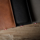 Three leather  iphone cases in brown, black, and gray on a wooden surface.