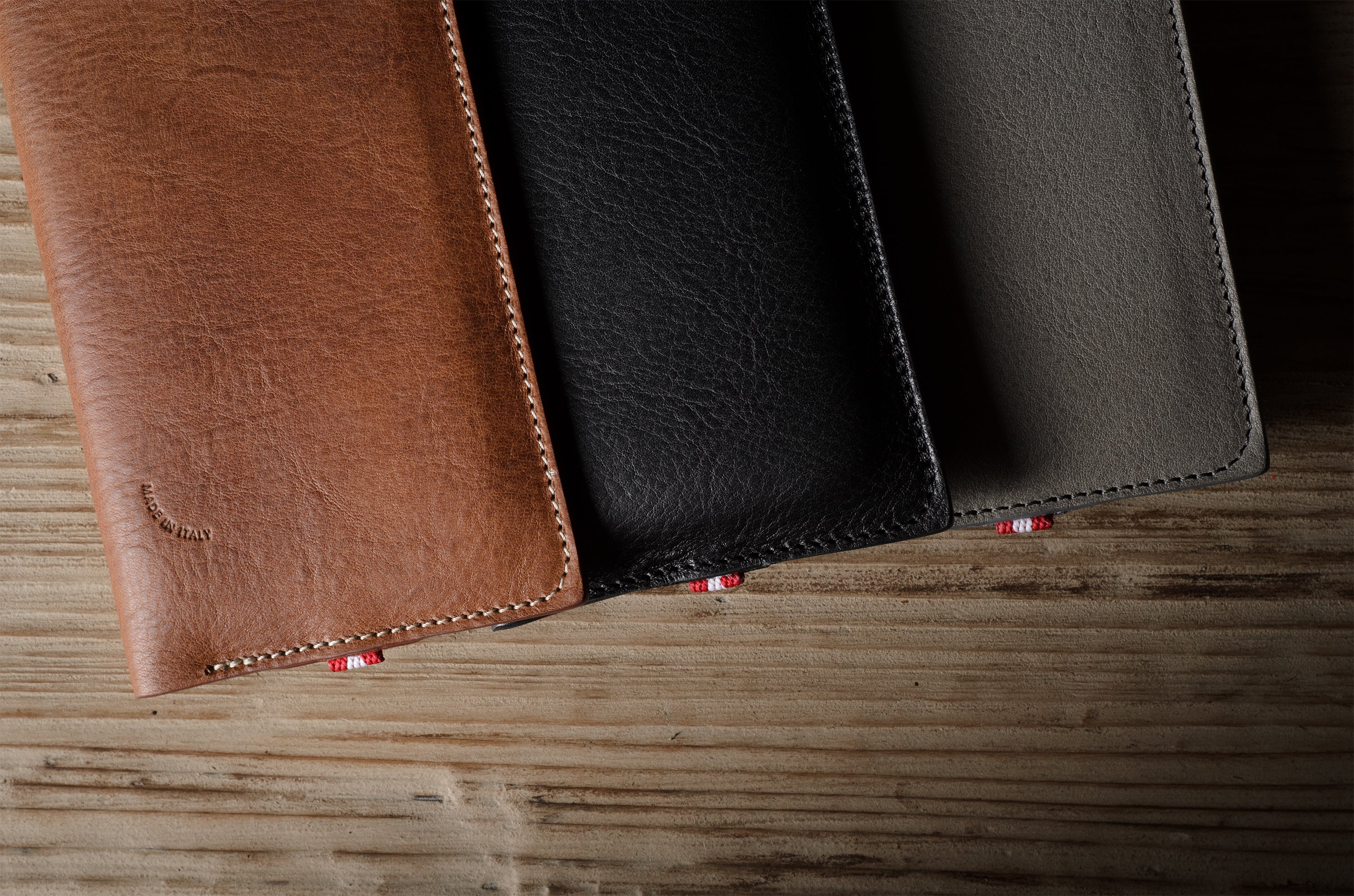 Three leather  iphone cases in brown, black, and gray on a wooden surface.