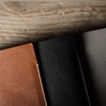 Three iphone cases in brown, black, and dark gray on a wooden surface.