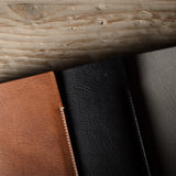 Three iphone cases in brown, black, and dark gray on a wooden surface.