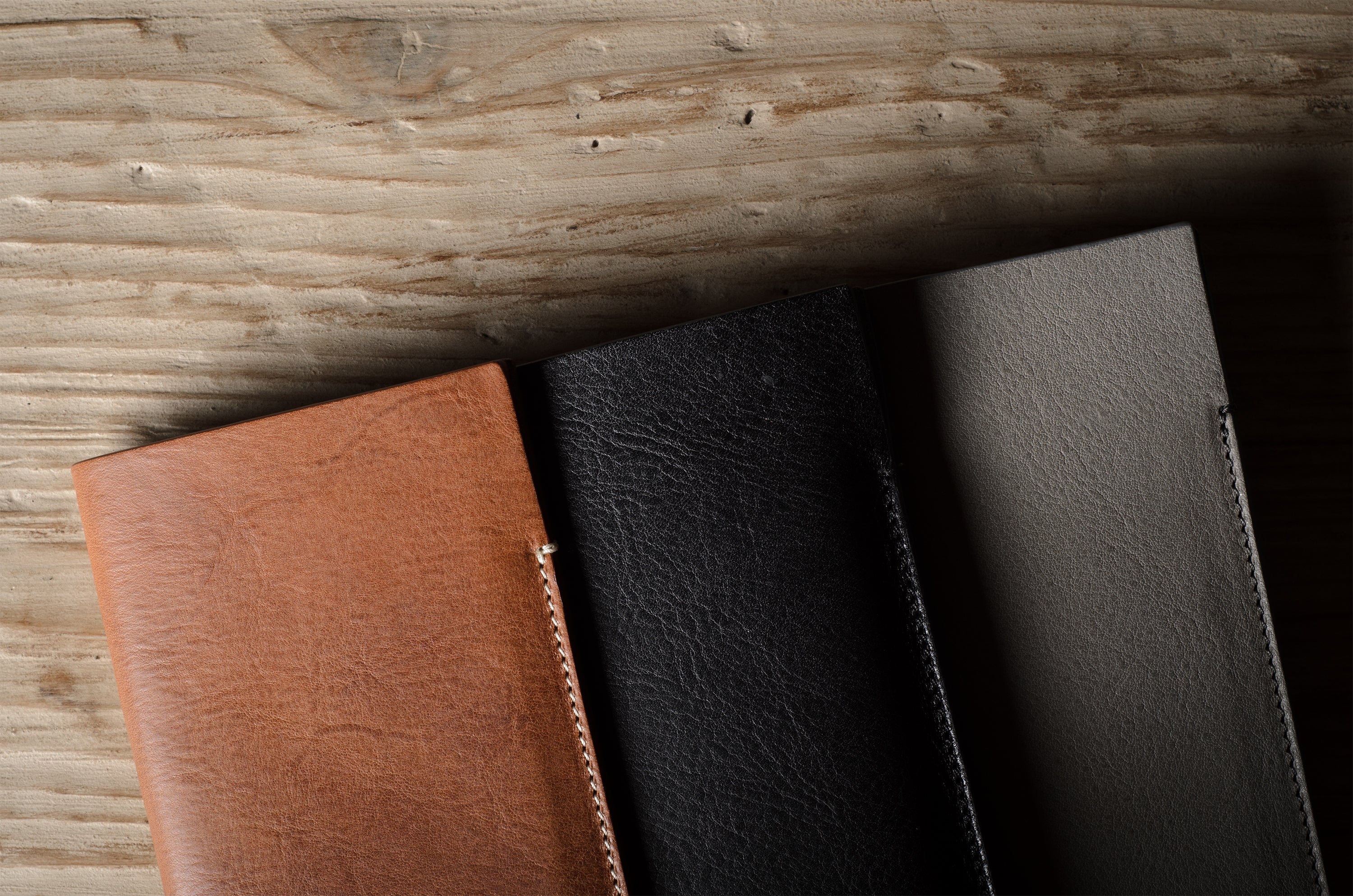 Three iphone cases in brown, black, and dark gray on a wooden surface.