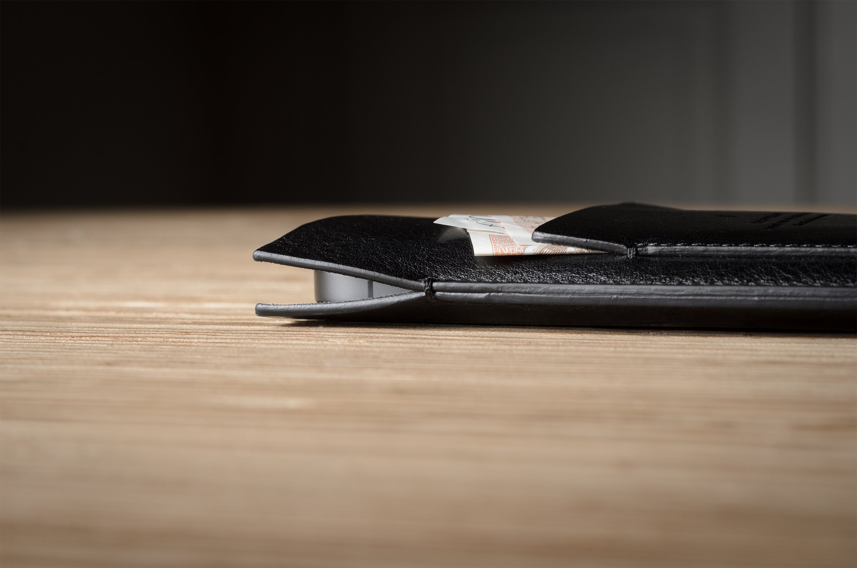 Close-up of a black leather iphone case on a wooden surface with a dark background