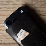 Black iphone case with a card holder attached to a smartphone on a wooden surface