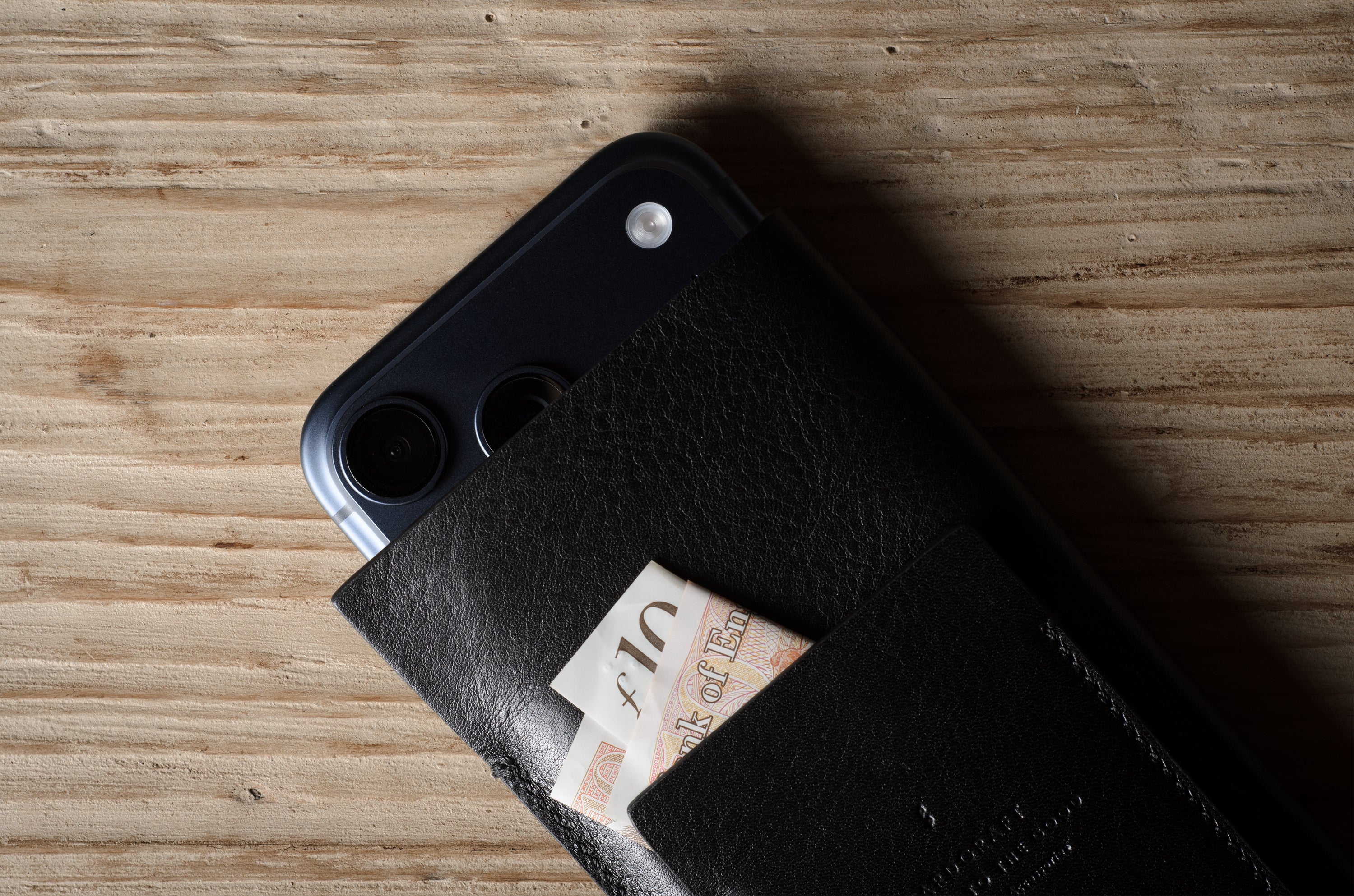 Black iphone case with a card holder attached to a smartphone on a wooden surface
