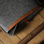 Gray wool felt laptop sleeve with brown leather on a wooden surface