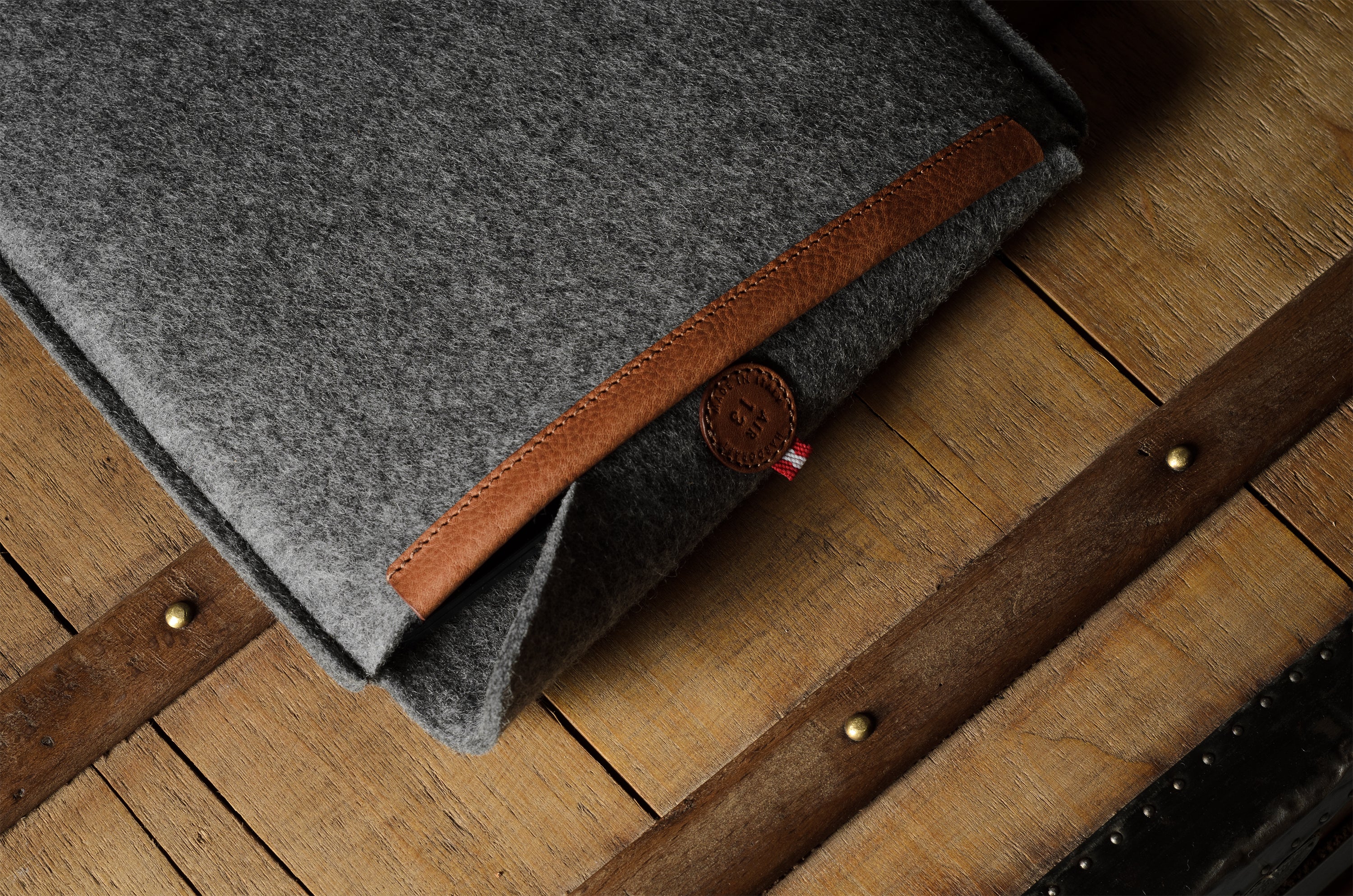 Gray wool felt laptop sleeve with brown leather on a wooden surface