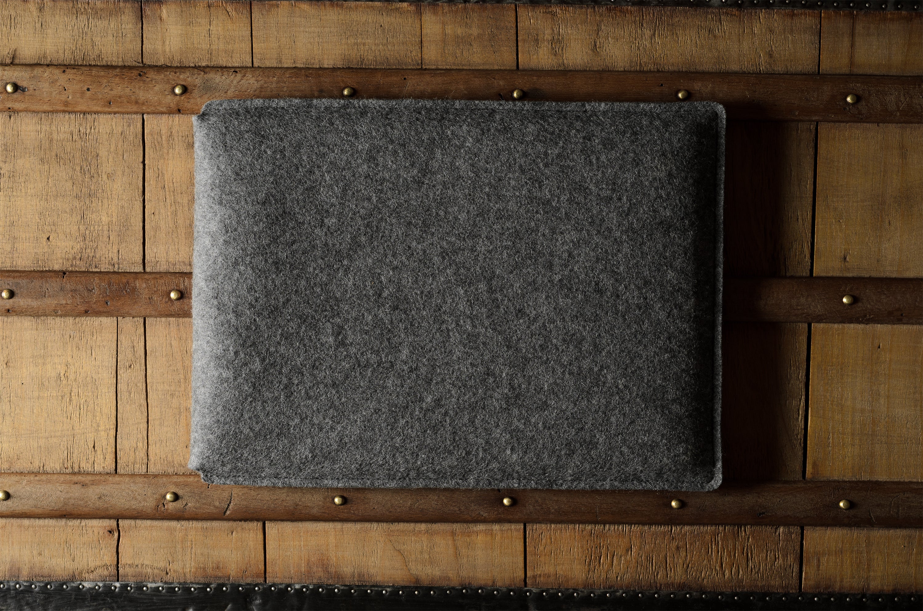 Gray wool felt laptop sleeve with brown leather on a wooden surface