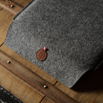 Gray wool felt laptop sleeve with brown leather on a wooden surface