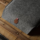 Gray wool felt laptop sleeve with brown leather on a wooden surface