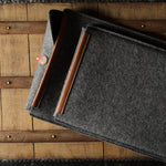 Gray wool felt laptop sleeve with brown leather on a wooden surface