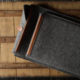 Gray wool felt laptop sleeve with brown leather on a wooden surface