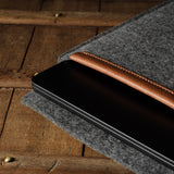Gray wool felt laptop sleeve with brown leather on a wooden surface