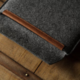 Gray wool felt laptop sleeve with brown leather on a wooden surface