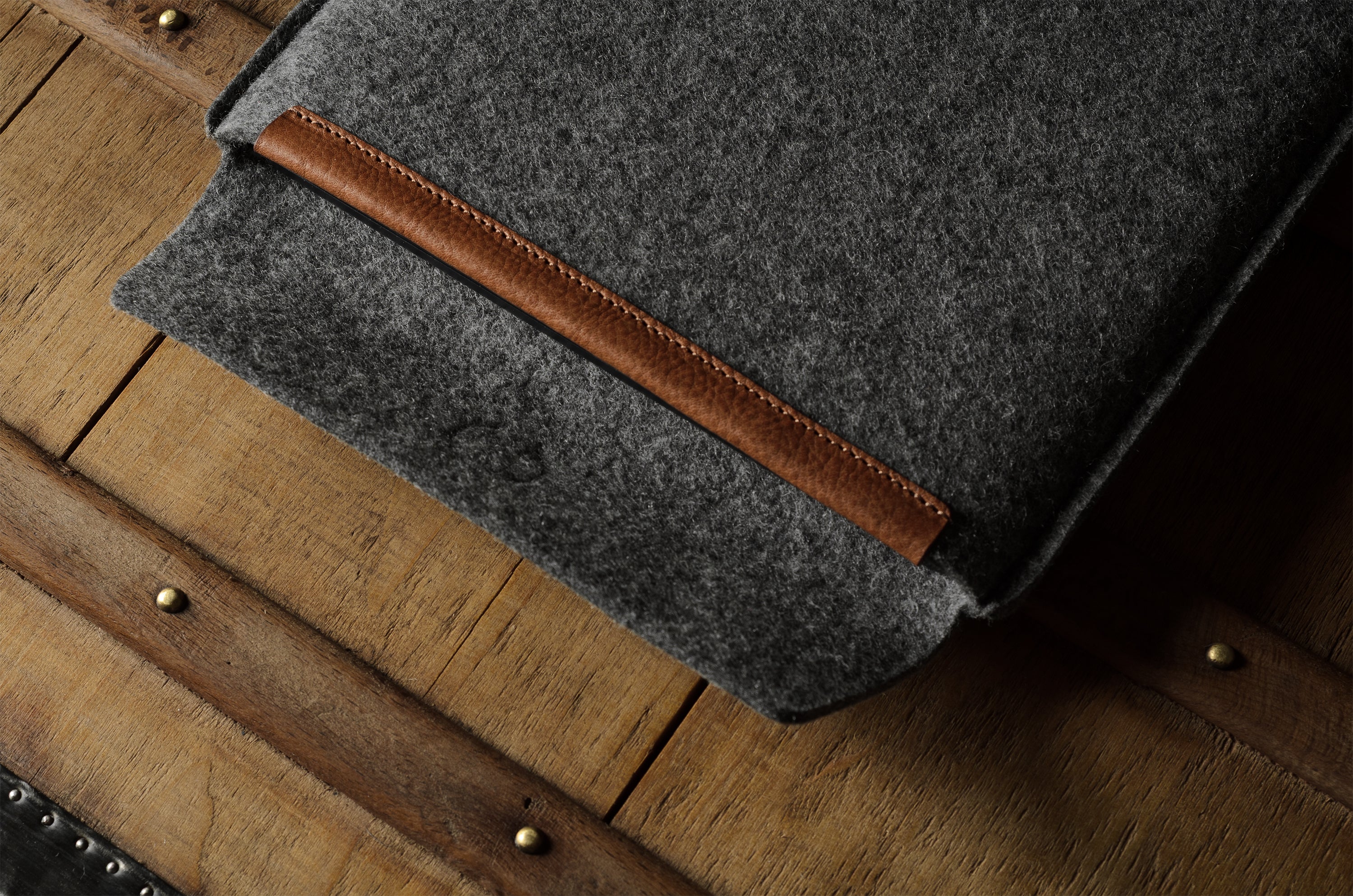 Gray wool felt laptop sleeve with brown leather on a wooden surface