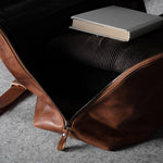 Brown leather bag with a book and sweater on a gray surface